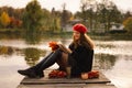 Woman in a red beret reading book on wooden pontoon. Autumn season. Royalty Free Stock Photo