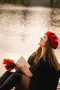 Woman in a red beret reading book on wooden pontoon. Autumn season. Royalty Free Stock Photo