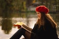 Woman in a red beret reading book on wooden pontoon. Autumn season. Royalty Free Stock Photo