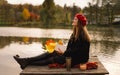 Woman in a red beret reading book on wooden pontoon. Autumn season. Royalty Free Stock Photo