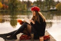 Woman in a red beret reading book on wooden pontoon. Autumn season. Royalty Free Stock Photo