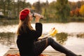 Woman in a red beret reading book on wooden pontoon. Autumn season. Royalty Free Stock Photo