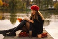 Woman in a red beret reading book on wooden pontoon. Autumn season. Royalty Free Stock Photo