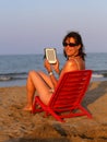 Woman on red chair reads the ebook on the beach by the sea in su Royalty Free Stock Photo