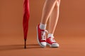Woman in red classic old school sneakers and umbrella on brown background, closeup