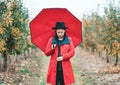 Woman in red coat and with umbrella between trees in apple garden at autumn season. Beautiful portrait of caucasian girl Royalty Free Stock Photo