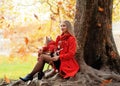 woman in red coat with yorkshire terrier sitting under the tree in autumn park Royalty Free Stock Photo