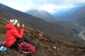 Woman in a red down jacket sits on the slope of mountain in Himalayas and drinks tea