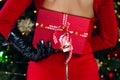 A woman in a red dress and black gloves holds a Christmas present in front of a decorated Christmas tree Royalty Free Stock Photo