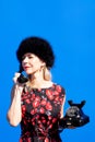 Woman in red dress and black hat with retro black phone on blue background Royalty Free Stock Photo