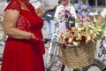 Woman in a red dress and gloves holds the bike wheel. Basket with roses. Frame part