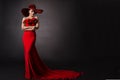 Woman Red Dress And Hat. Fashion Model In Long Evening Gown With Flowers. Black Studio Background