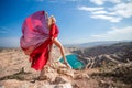 woman red dress lake mountains. Side view of a woman in a long red dress posing on a rock high above the lake. Against Royalty Free Stock Photo