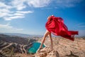 woman red dress lake mountains. Side view of a woman in a long red dress posing on a rock high above the lake. Against Royalty Free Stock Photo