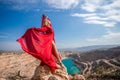 woman red dress lake mountains. Side view of a woman in a long red dress posing on a rock high above the lake. Against Royalty Free Stock Photo