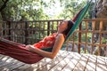 A woman in a red dress lies in a hammock on the terrace of a wooden house and enjoys the view Royalty Free Stock Photo