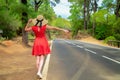 Woman in red dress by the road in forest trying to hitchhike a ride.