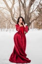 woman in a red dress of the Rococo era stands in the snow against the background of a winter forest Royalty Free Stock Photo