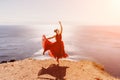 Woman red dress sea. Female dancer in a long red dress posing on a beach with rocks on sunny day. Girl on the nature on Royalty Free Stock Photo