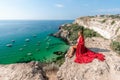 Woman red dress sea. Happy woman in a red dress and white bikini sitting on a rocky outcrop, gazing out at the sea with Royalty Free Stock Photo