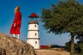 A woman in a red dress is standing on the beach near the lighthouse at sunrise Royalty Free Stock Photo