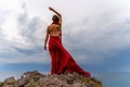 A woman in a red dress stands above a stormy sky, her dress fluttering, the fabric flying in the wind. Royalty Free Stock Photo