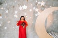 A woman in a red dress stands and holds a bouquet of red roses and strawberries in a fabulous studio