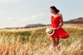 Woman in a red dress walking on the field on a warm summer evening. Yellow grass at sunset, the girl holding a hat in his hands Royalty Free Stock Photo