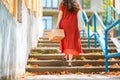 A woman in a red dress walks up the steps with a parcel in her hand. Rear view. Close up. The concept of delivery of goods