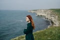 Woman with red hair on a cliff of a mountain by the sea, wind, smile Royalty Free Stock Photo