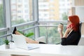 Woman with red hair is drinking coffee and talking on the phone at the workplace in the office Royalty Free Stock Photo