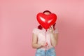 woman with red hair hides face behind large flying red heart-shaped balloon in hands , isolated on a pink background Royalty Free Stock Photo