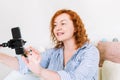 A woman with red hair holds a phone on a selfie stick and records a vertical video for stories on social networks.