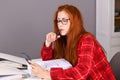 Woman with red hair sitting at desk with document ring files looking at mobile phone Royalty Free Stock Photo