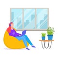 Woman with red hair sitting on yellow beanbag using laptop, indoor with large window, modern workspace. Freelancer