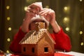 Woman in red hat building gingerbread house.