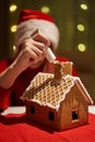 Woman in red hat building gingerbread house.