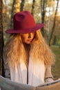 A woman in a red hat reads a newspaper standing near a tree