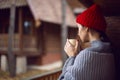 woman in a red hat and scarf and a mug stands at a wooden house in the woods Royalty Free Stock Photo