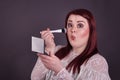 Woman applying makeup with brush puckering lips holding compact mirror