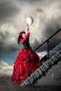 Woman in a red historical dress is catching a white balloon.