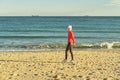 A woman in a red jumper and white hat walks along the sandy beach. Royalty Free Stock Photo