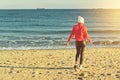 A woman in a red jumper and white hat walks along the sandy beach. Royalty Free Stock Photo