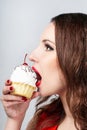 Woman with red lips eating a cake with cream and a cherry on the light background. Delicious cupcake in a womans hand close-up Royalty Free Stock Photo