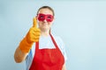 Woman in red mask, gloves and apron showing thumb up. Super housewife