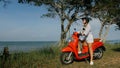 Woman on red motorbike in white clothes drive on forest road trail trip. One girl caucasian tourist go on scooter Royalty Free Stock Photo