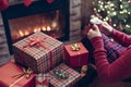 Woman with red mug of hot chocolate and melted marshmallow packing handmade christmas gifts sitting near christmas tree