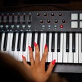Woman with red nails playing electronic musical keyboard synthesizer