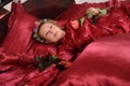 Woman in red pajamas lying on a bed on silk red linen with hair curlers and a rose in her hand Royalty Free Stock Photo