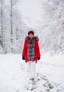 A woman in a red quilted jacket is standing in a snowy forest.